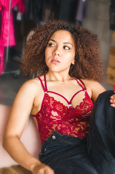 Model in red lace bodysuit and unbuttoned jeans, showcasing curly hair and fashion style.
