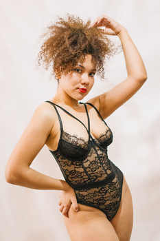 Fashionable woman in black lace bodysuit posing confidently indoors. Studio photography.