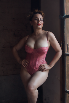 Stylish woman in pink lingerie poses confidently by a window, showcasing modern fashion.