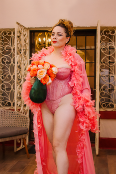 Stylish woman in pink lace lingerie holding roses, exuding elegance and confidence indoors.