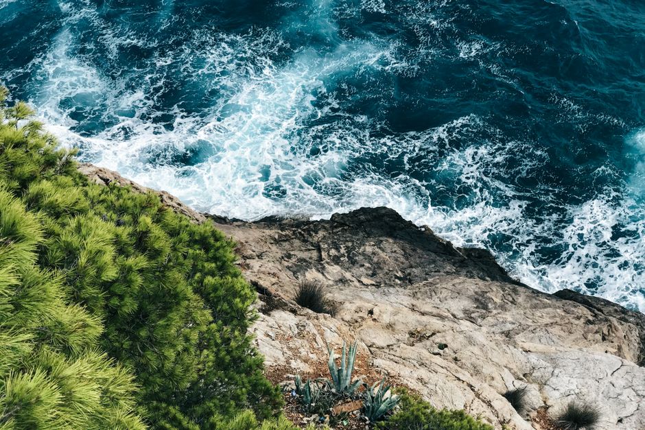 Vibrant seascape showcasing the rugged coastline of Son Servera, Spain with lush greenery and crashing ocean waves.