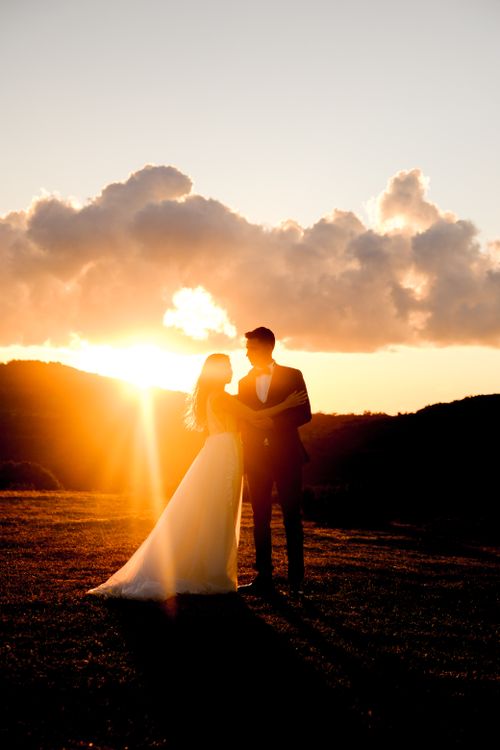 Free A couple embraces at sunset in a scenic countryside field, perfect for wedding themes. Stock Photo