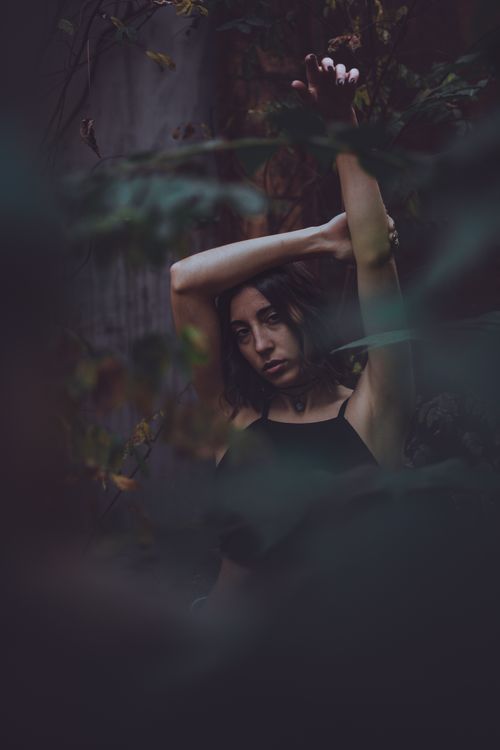 Free Artistic portrait of a woman in a forest with raised arms, creating a mysterious and moody atmosphere. Stock Photo