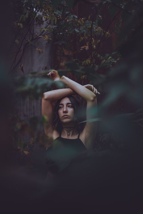 Free A serene portrait of a woman with arms raised among lush forest foliage. Stock Photo