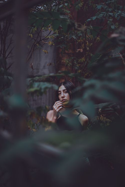 Free A contemplative woman stands amidst dense forest foliage, creating a moody and intimate ambiance. Stock Photo