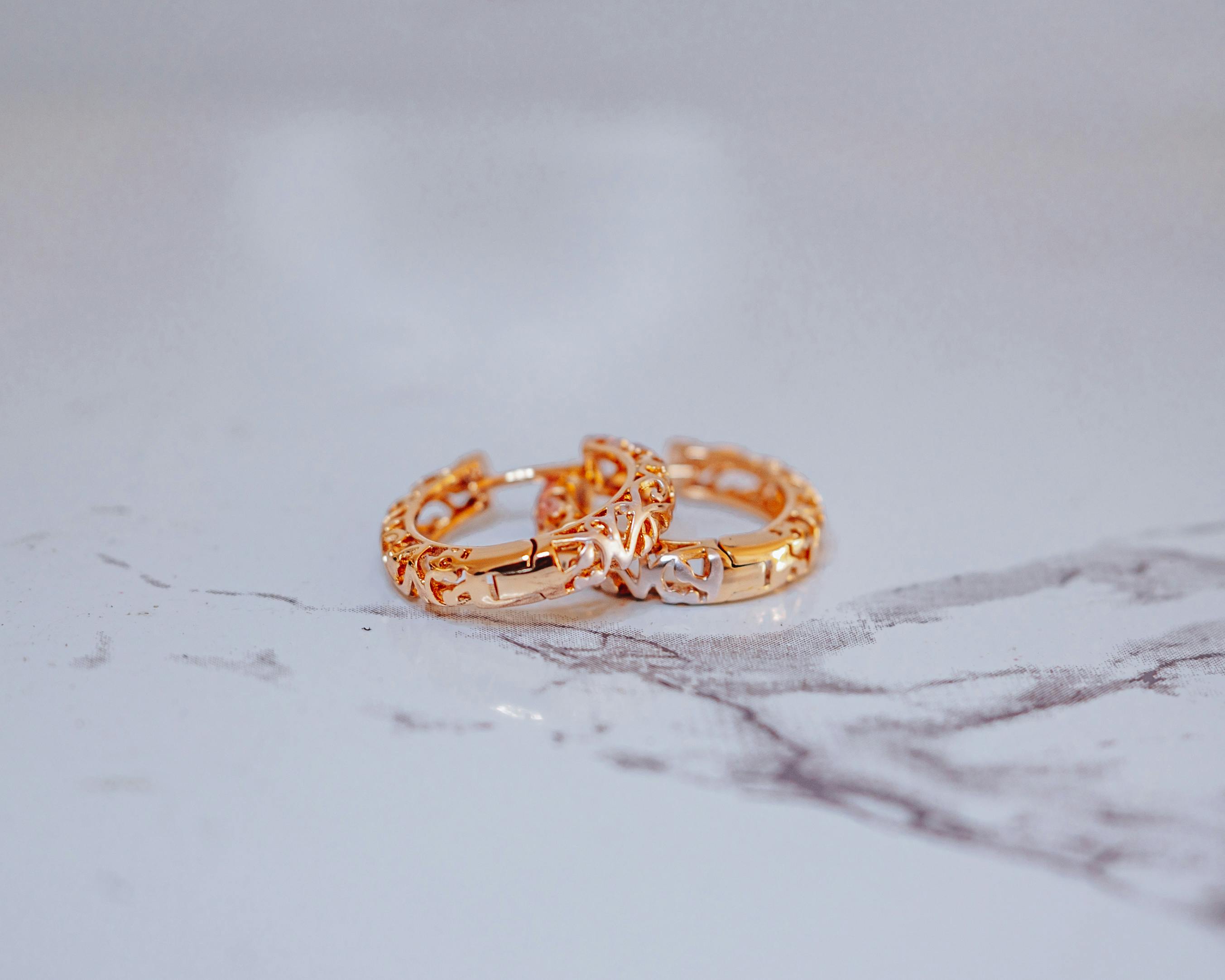 two gold rings with diamonds on top of a marble surface