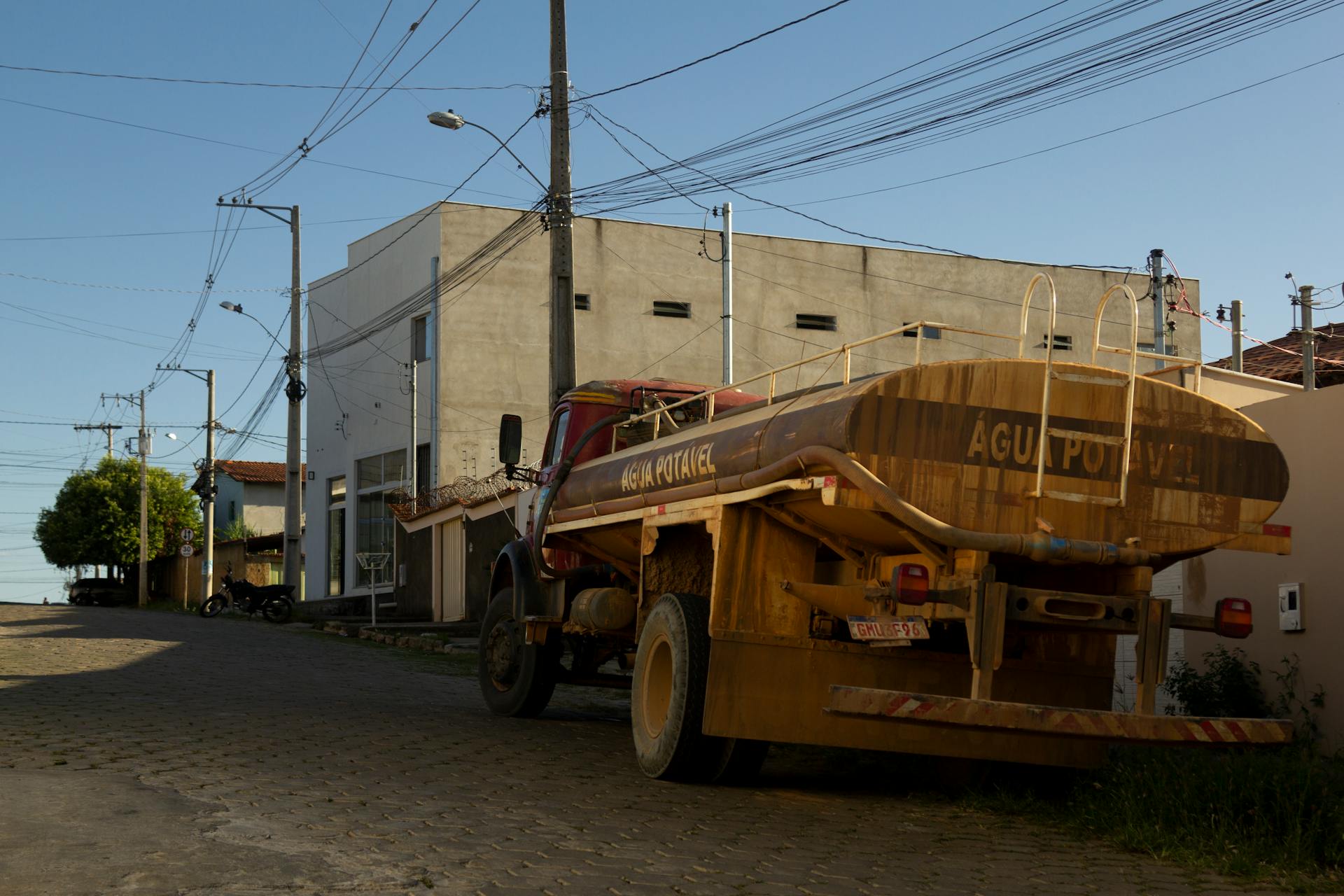 A street view of a rural area showing a water tank truck and utility poles with power lines.