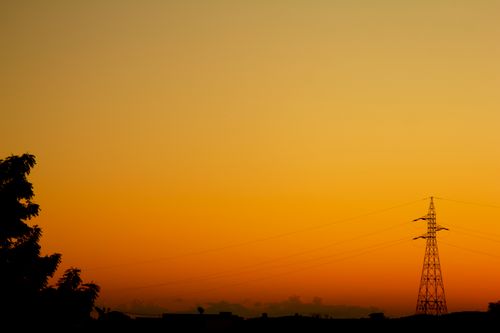 Free Silhouette of a power line tower against a vibrant orange sky during sunset. Stock Photo
