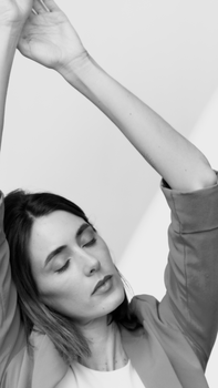 Black and white portrait of a woman with closed eyes, raising hands, wearing a blazer.