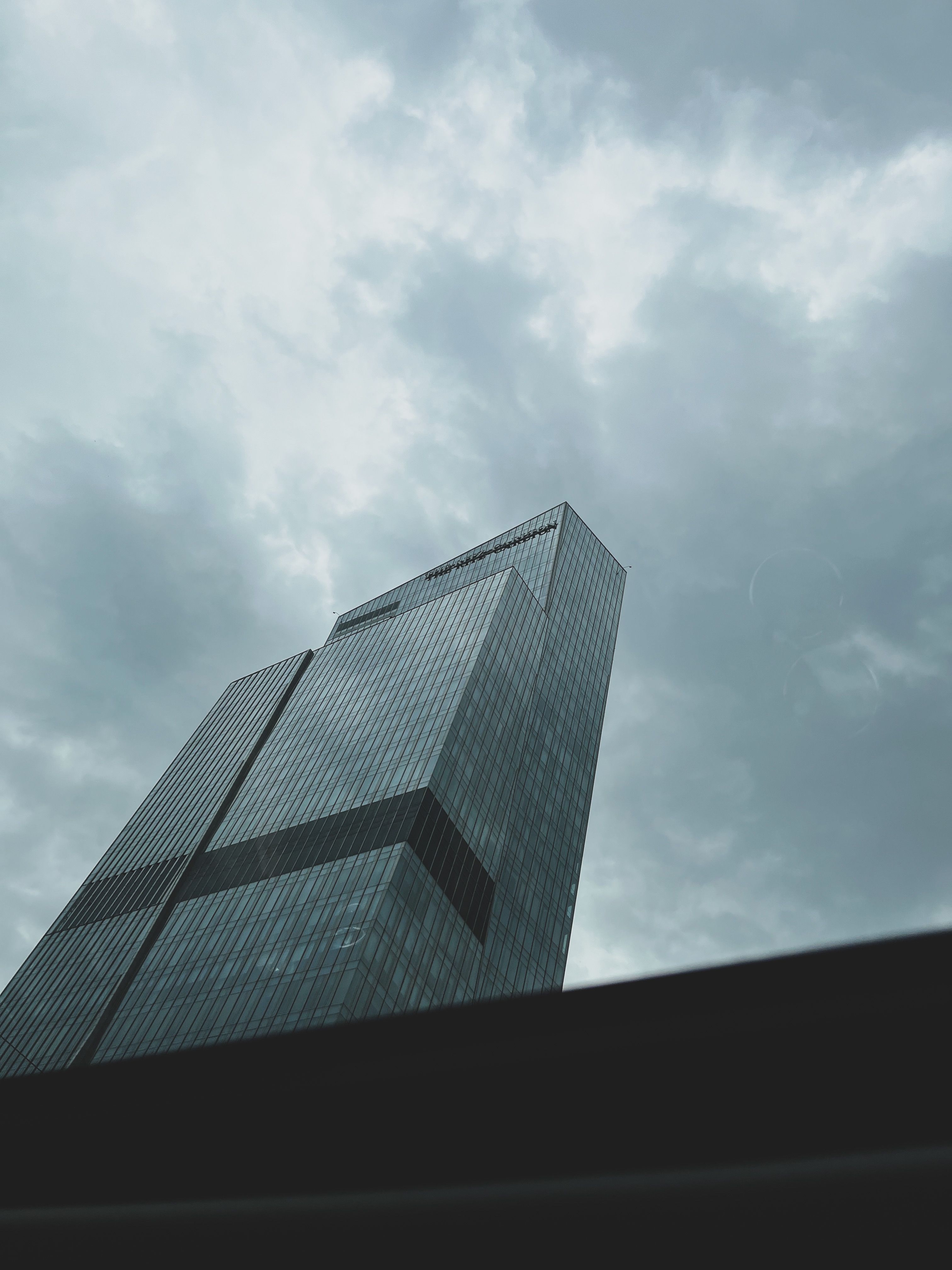 Low angle view of a modern skyscraper against a dramatic overcast sky.
