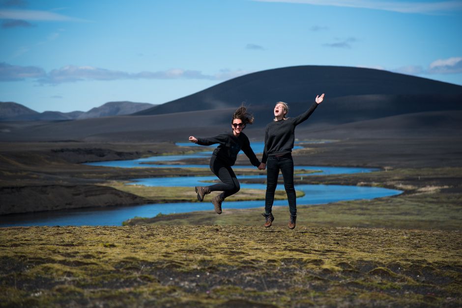 Two friends jump with joy in a stunning Icelandic mountain landscape.