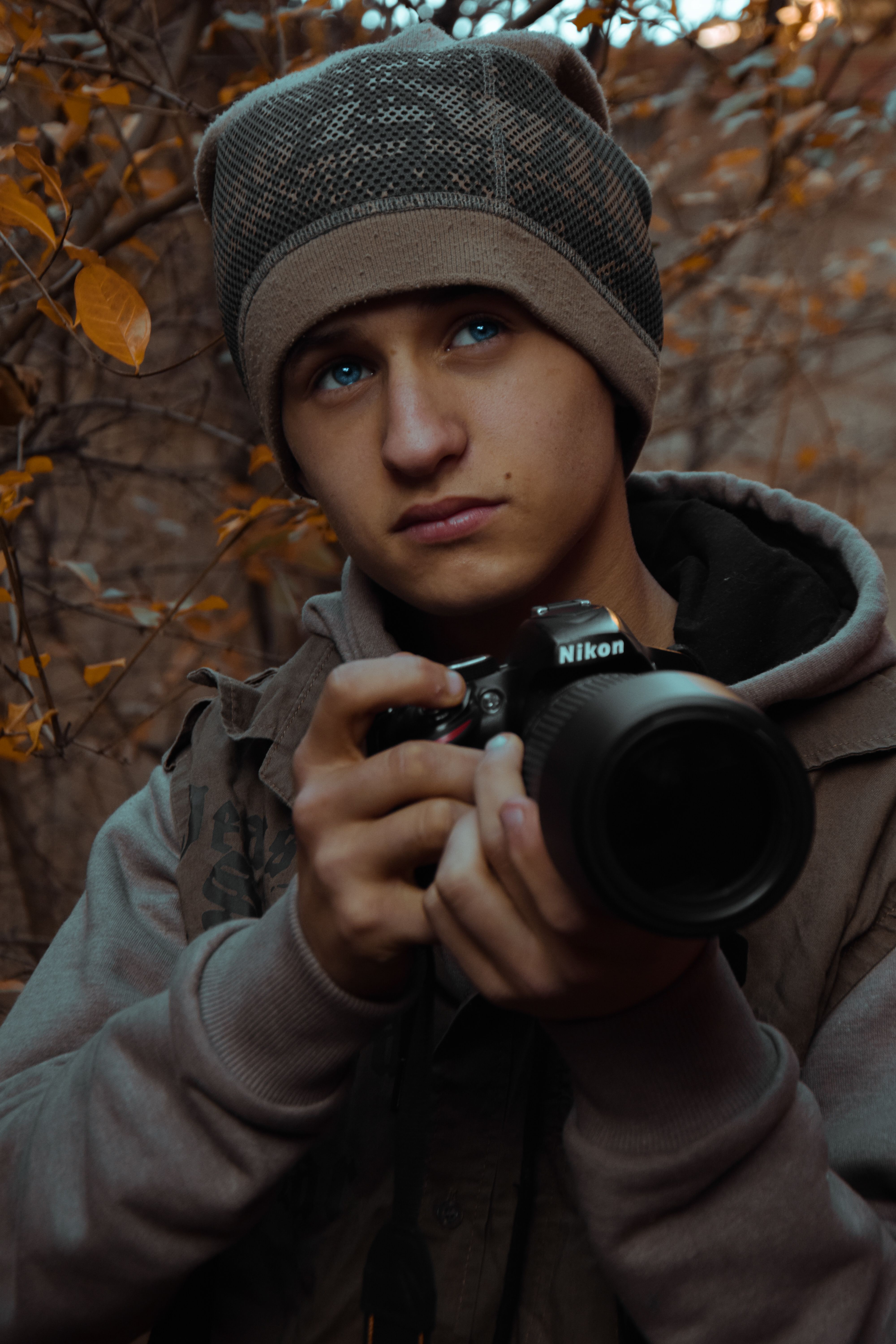 A young man holding a Nikon camera in an autumn forest setting.