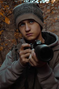 A young man holding a Nikon camera in an autumn forest setting.