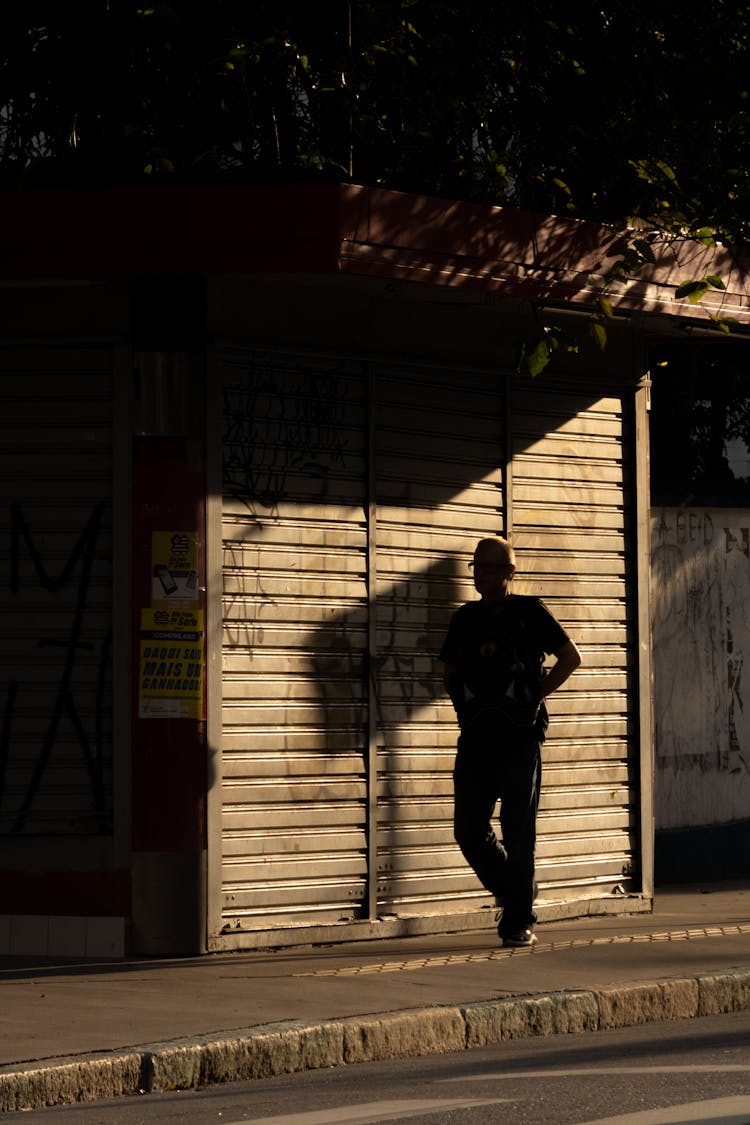 Silhouette Of Man Leaning On Closed Kiosk With Newspapers