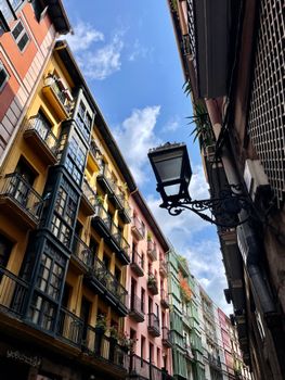Vibrant facades line a narrow Bilbao street under a bright blue sky.