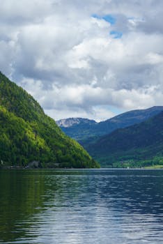 A serene view of Hallstatt Lake with lush green mountains under a cloudy sky.