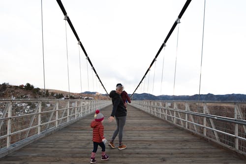 Woman Carrying Child Walking Along Bridge