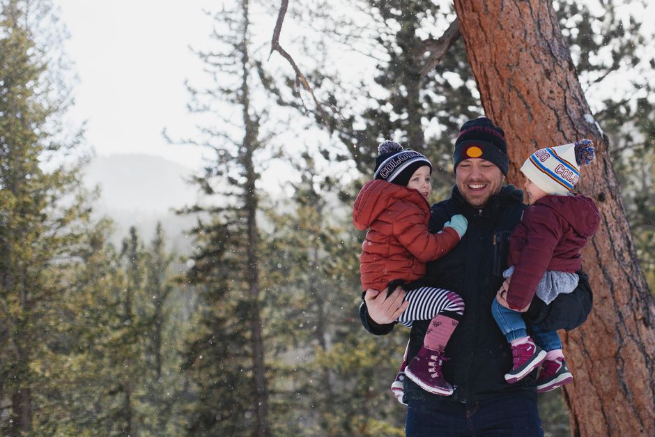 A joyful father holding his children in a snowy forest during winter, creating lasting memories.