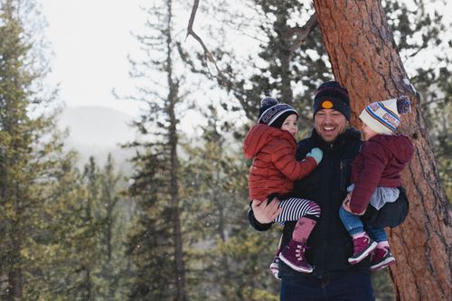 Free A joyful father holding his children in a snowy forest during winter, creating lasting memories. Stock Photo