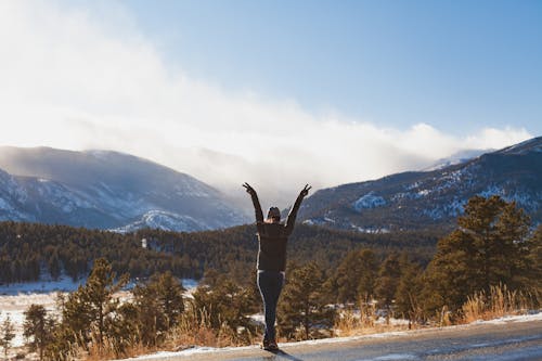 Person Raising Hands on Road Across Mountain Range