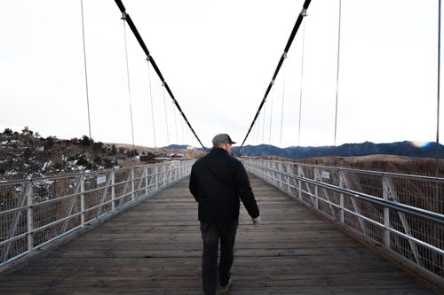 Free A man walks across a scenic suspension bridge in a mountainous valley, showcasing adventure and exploration. Stock Photo