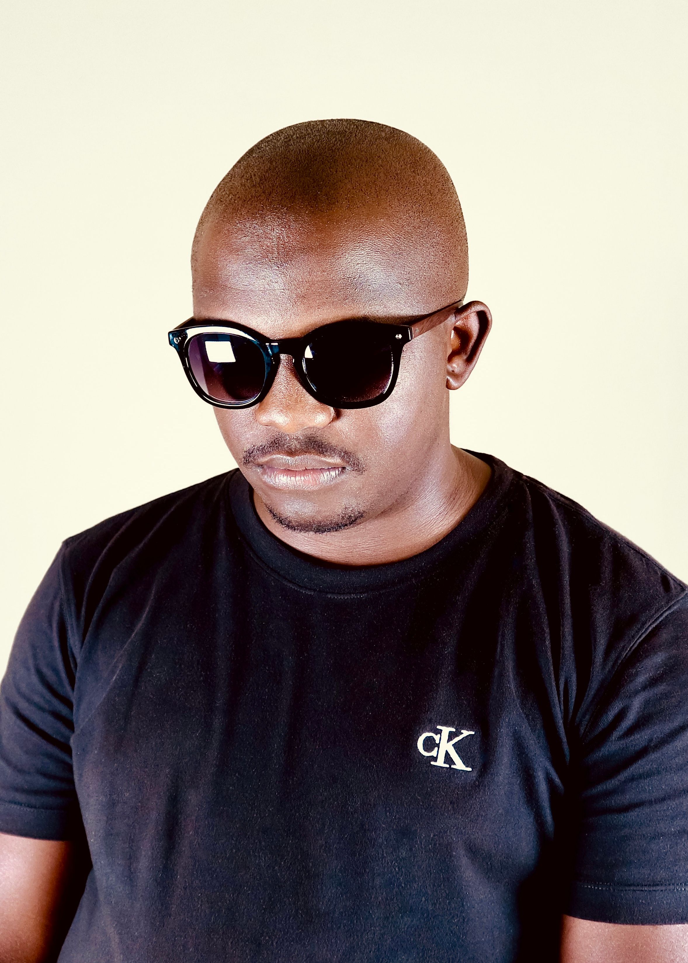Studio portrait of a bald man wearing sunglasses and a black T-shirt with logo.