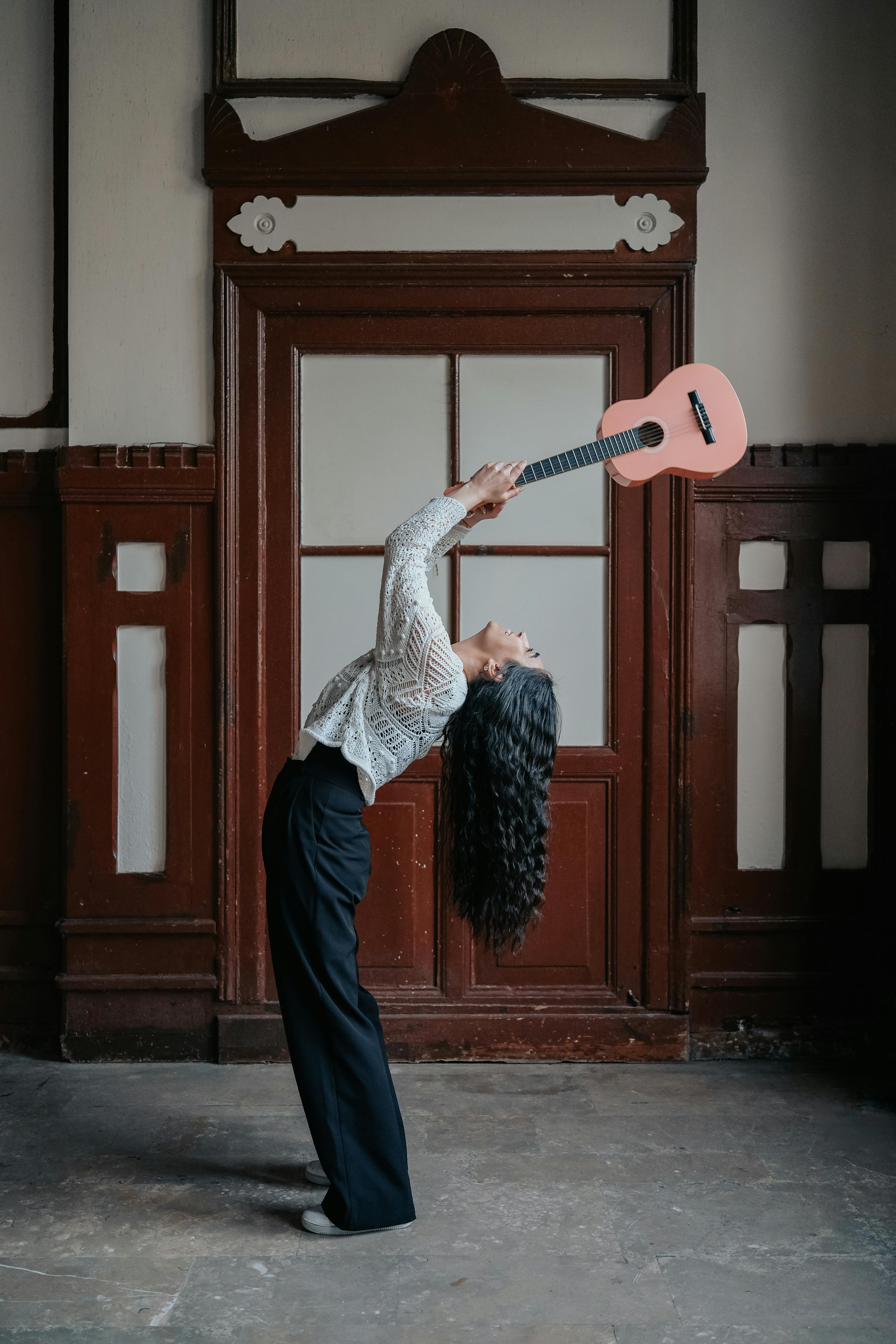 Artistic shot of a woman leaning back holding a ukulele in an elegant pose indoors.