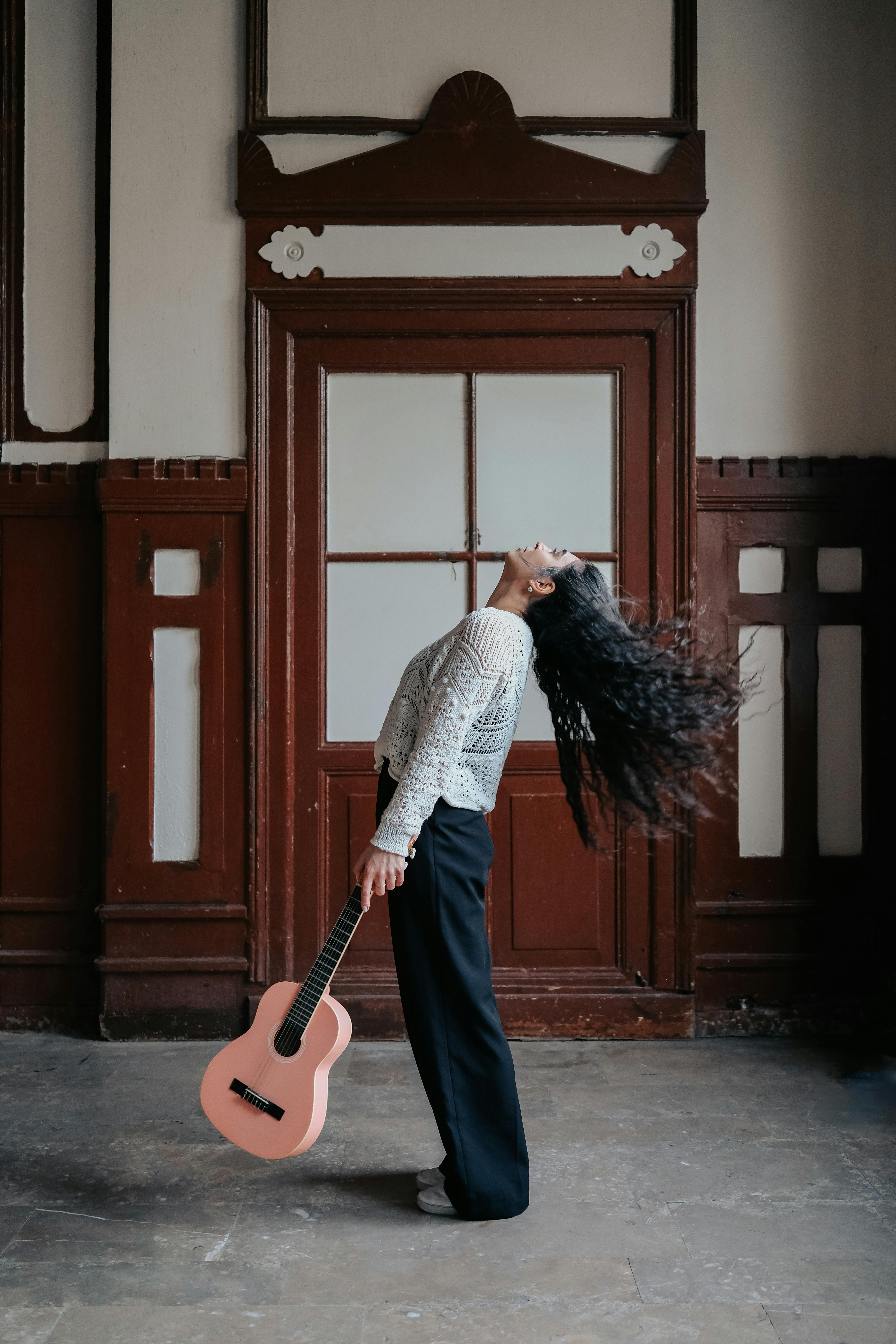 Woman posing indoors holding a guitar, showcasing fashion and music theme.
