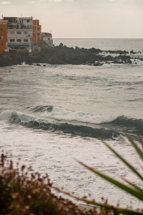 Free View of ocean waves crashing near coastal houses with rocky shorelines at sunrise. Stock Photo
