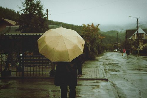 Free A person walks under an umbrella on a rainy city street, evoking a moody atmosphere. Stock Photo