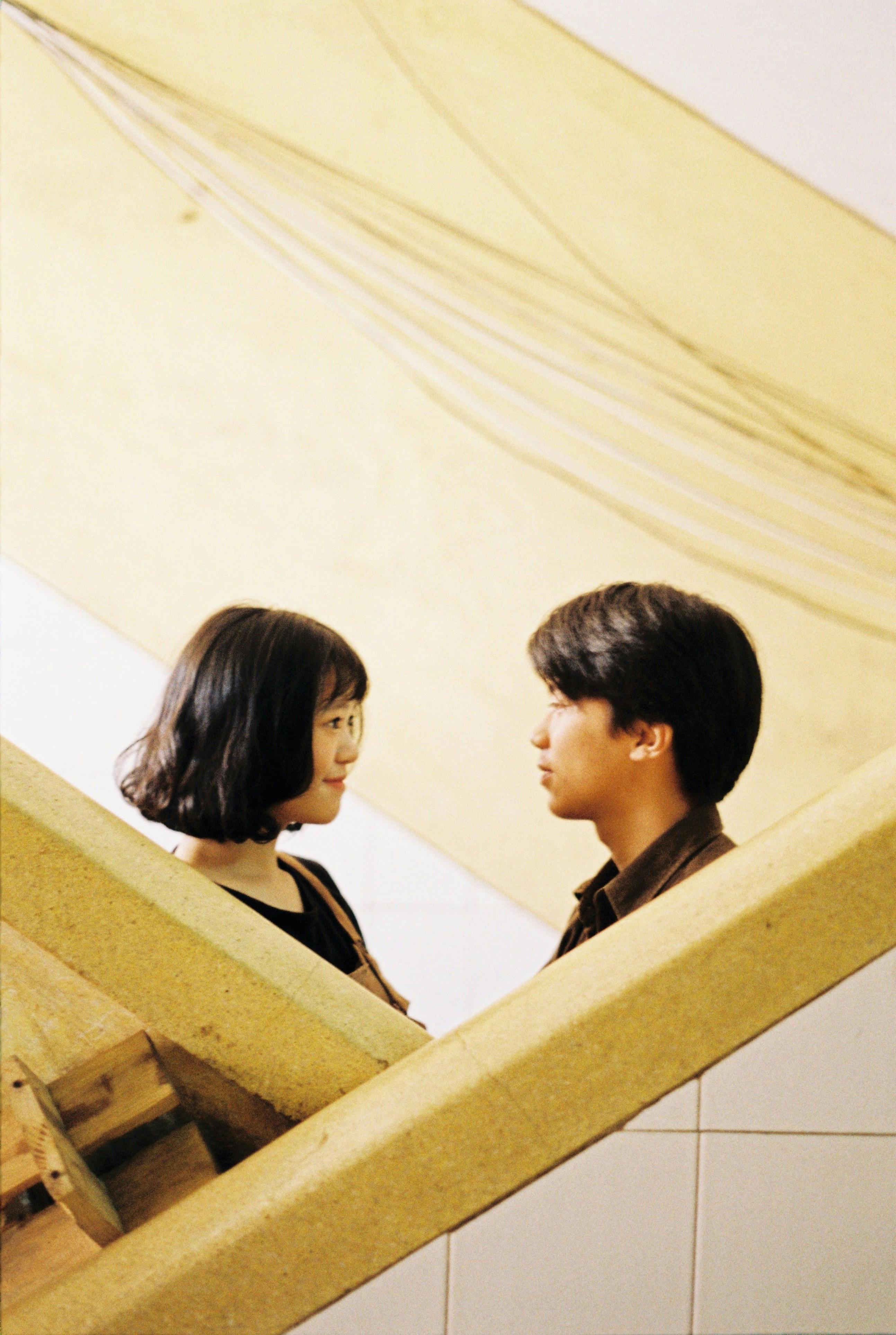 Man and woman share a thoughtful gaze on indoor yellow staircase.