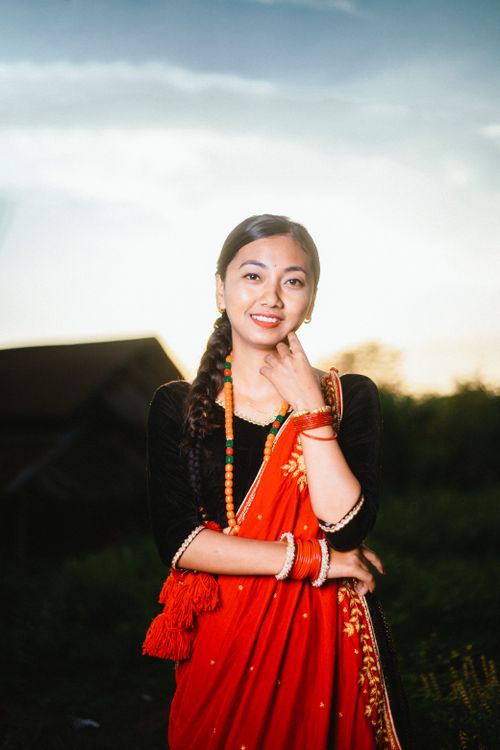 Free Portrait of a smiling woman in a red saree and jewelry outdoors at sunset. Stock Photo