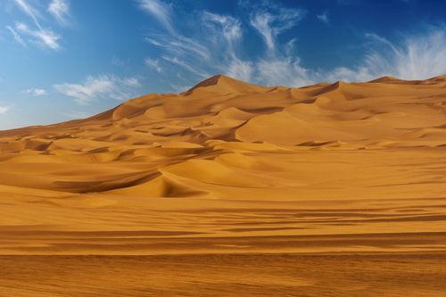 Free Majestic golden sand dunes stretch under a vibrant blue sky in a serene desert landscape. Stock Photo