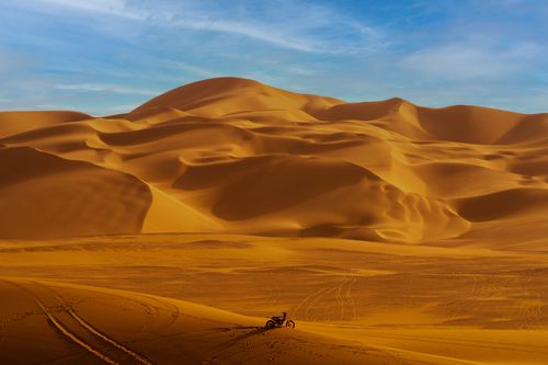 Free Majestic desert landscape with golden dunes and a lone motorcycle under blue skies, perfect for travel enthusiasts. Stock Photo