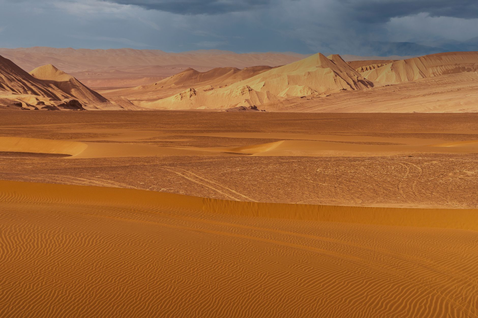 Stunning aerial shot of two cars making tracks on vibrant red sand dunes in a desert landscape.
