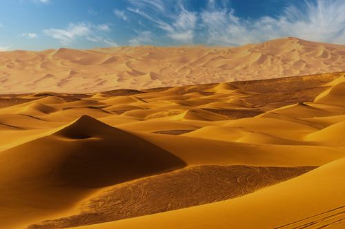 Free Stunning view of endless golden sand dunes under a bright blue sky, capturing the beauty of nature's vastness. Stock Photo
