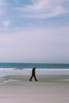 A solitary man in a hat walks on a serene beach with waves in Tijuana, Mexico.