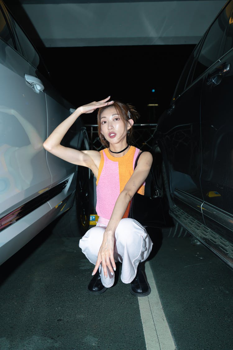 Young Woman In A Fashionable Outfit Posing Between Cars At The Parking Lot 