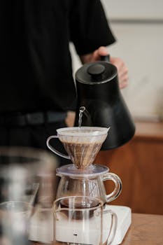 Close-up of a barista using a kettle for pour-over coffee brewing in a cafe setting.