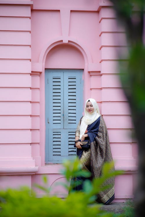 Young Woman Wearing Elegant Traditional Clothing and Standing by a Pink Wall 