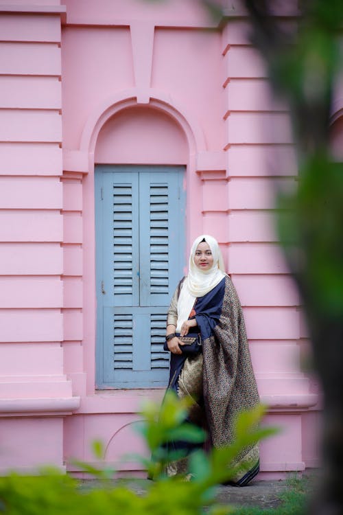 Young Woman Wearing Elegant Traditional Clothing and Standing by a Pink Wall 