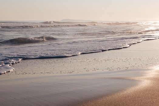Serene ocean waves gently washing onto a sandy beach during sunset, creating a tranquil coastal scene.