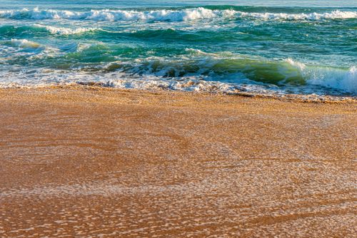 Free Peaceful waves crashing on a sandy shore under clear skies, perfect for beach lovers. Stock Photo