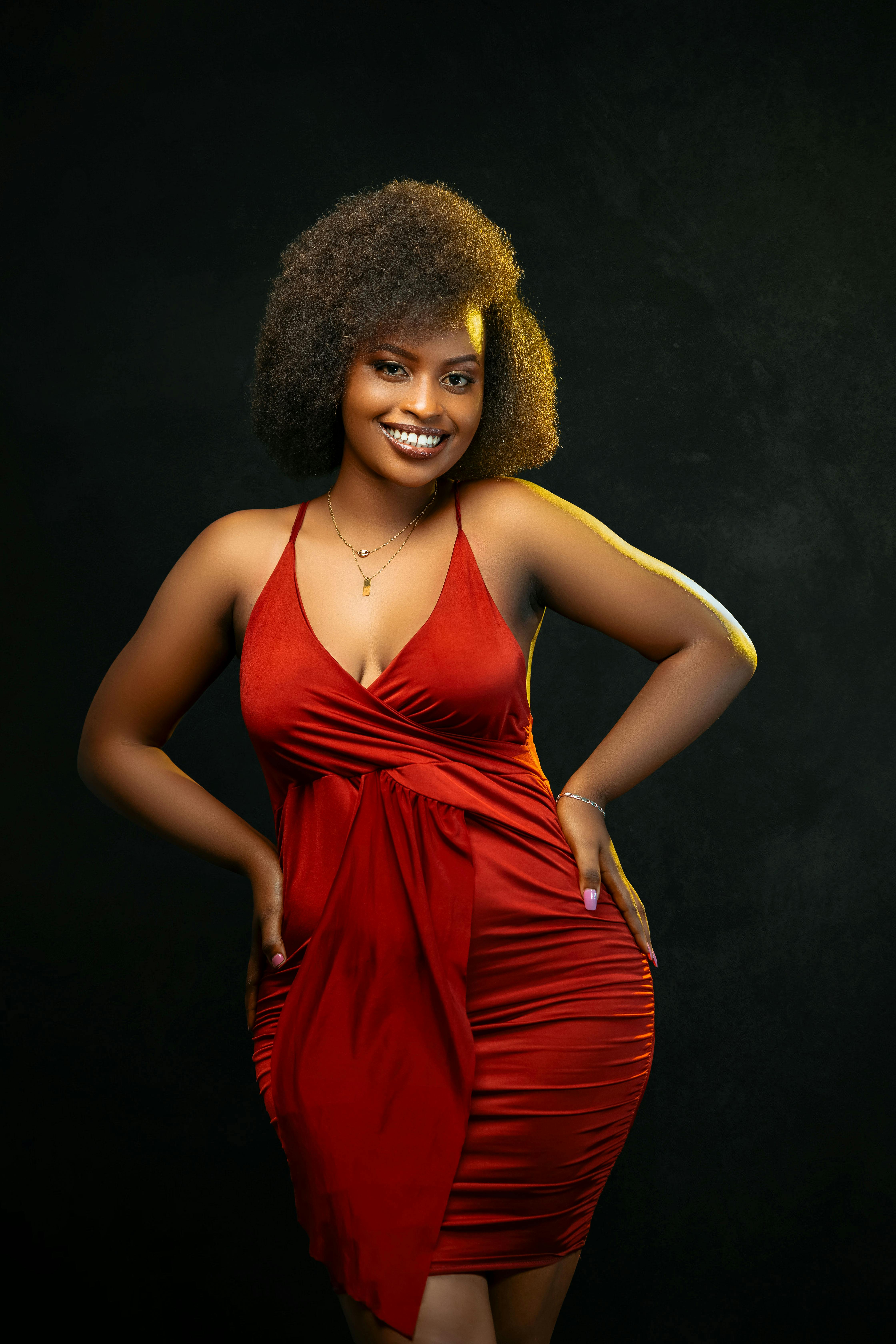 Stylish portrait of a smiling woman in a red dress with curly hair against a dark backdrop.