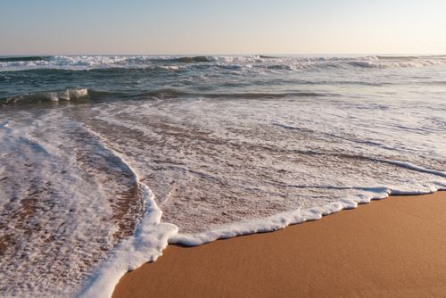 Free Serene ocean waves gently wash over a sandy beach at sunset, creating a peaceful seaside scene. Stock Photo