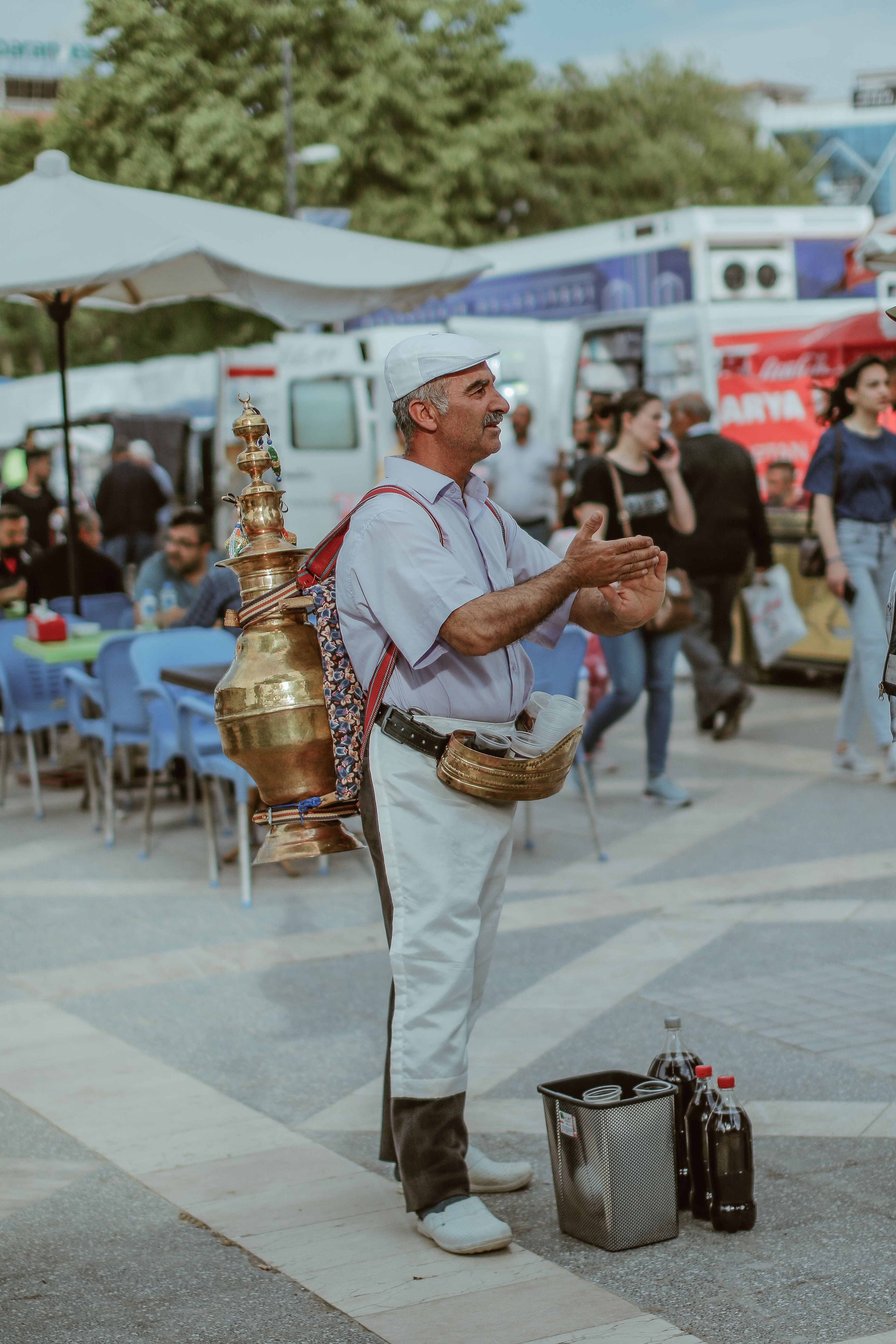 A tea seller stands with a brass urn in a Turkish city square, offering traditional drinks.
