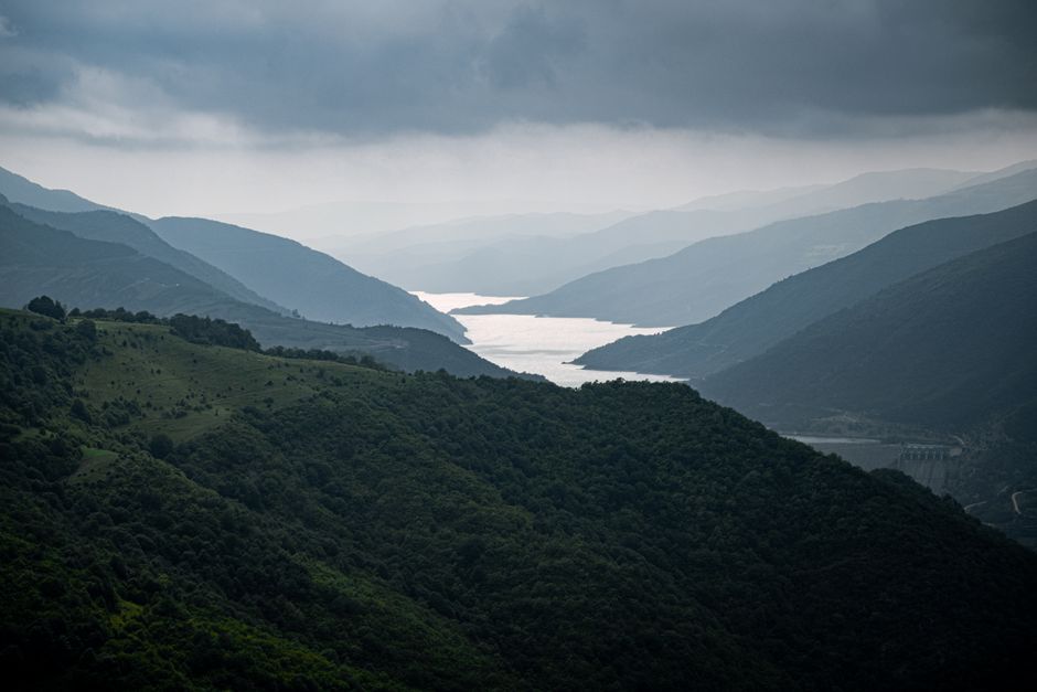 Majestic aerial view of a distant lake surrounded by lush green hills and misty mountains.