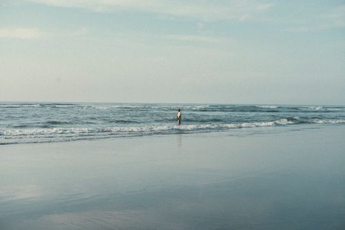 Free A peaceful beach scene with a person walking along the water's edge under a bright sky. Stock Photo