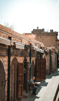 A serene view of a historical street with stone buildings and a seated elderly man under a sunny sky.