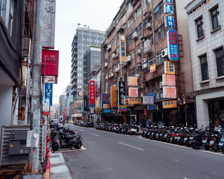 Street view of an Asian city with parked scooters and colorful signboards lining contemporary buildings.